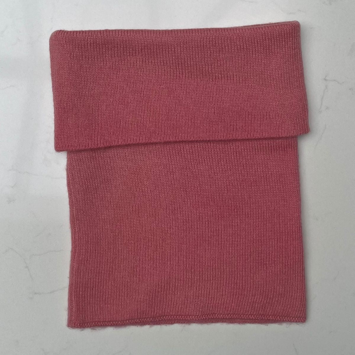 Folded pink cashmere snood on a light gray background