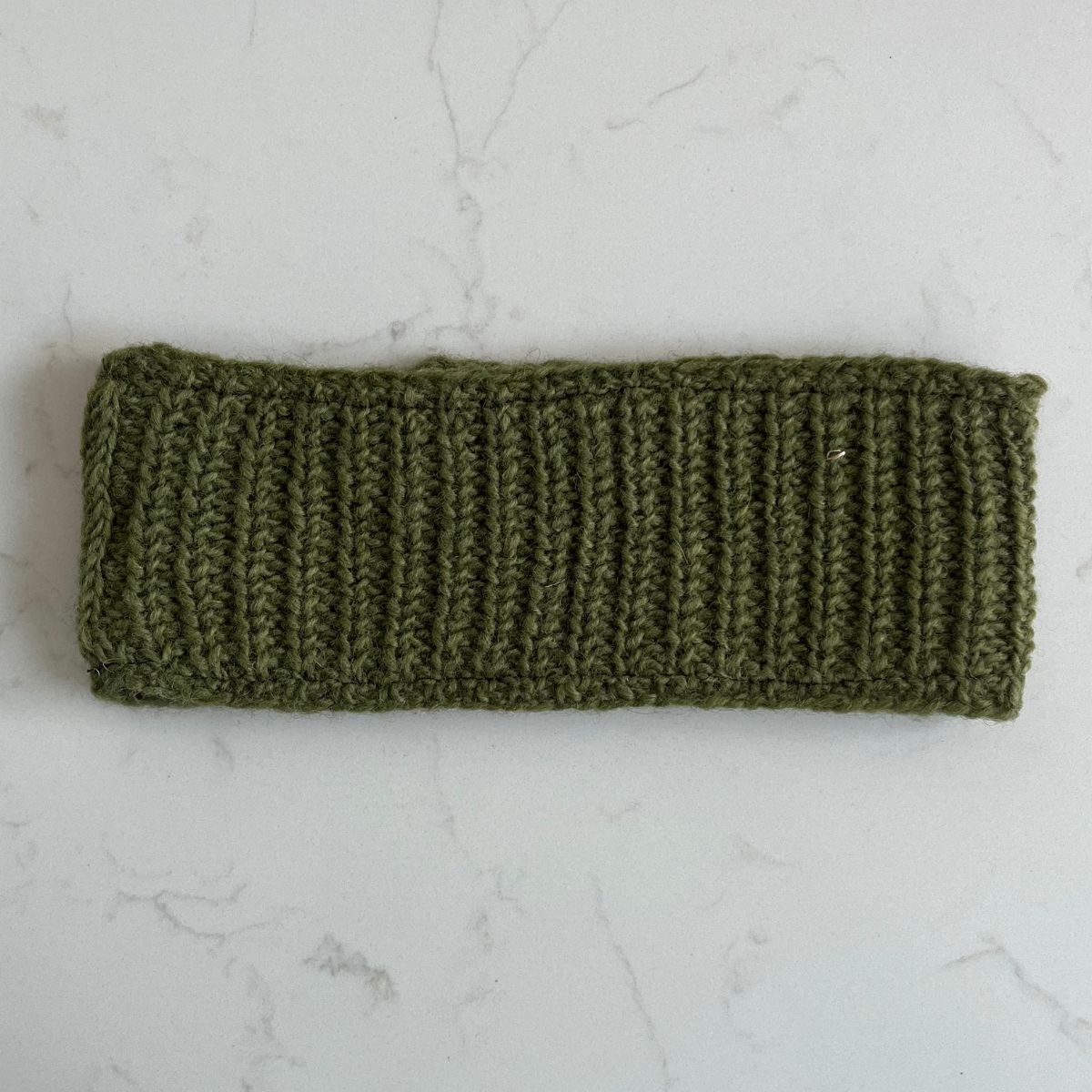 Khaki green plain knitted woollen headband with fleece lining on a light gray marble background
