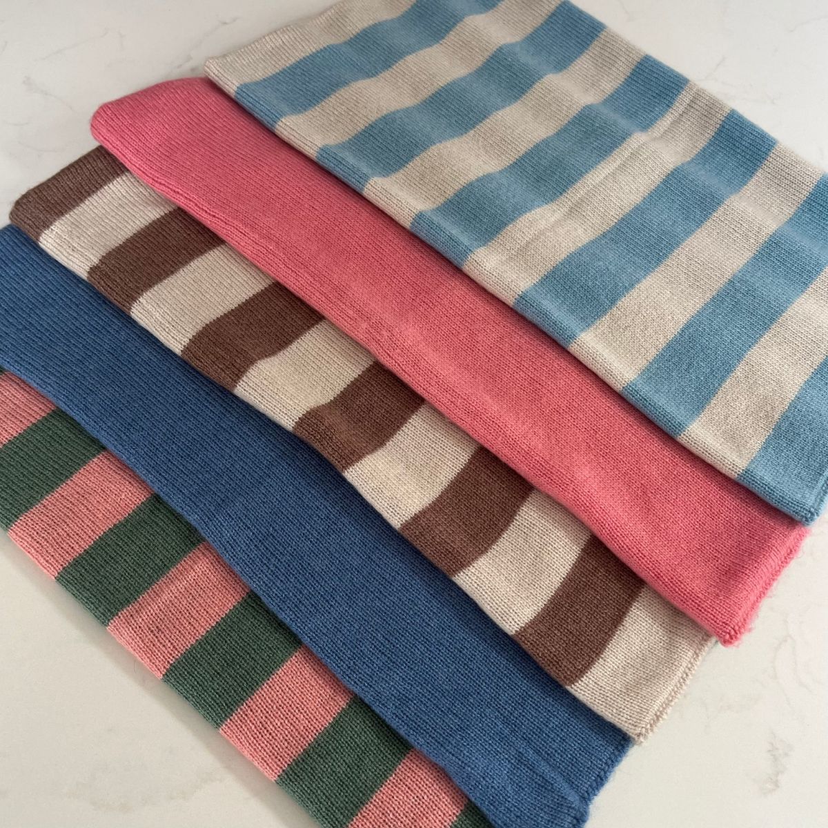 Stack of reversible cashmere snoods in various colors on a light background
