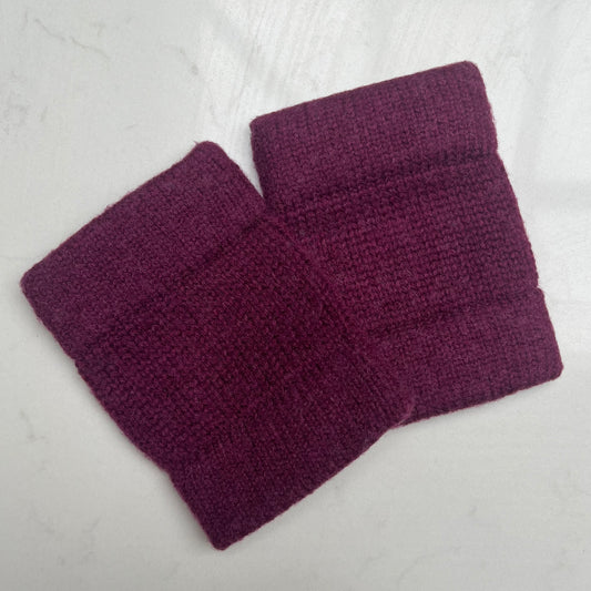 A pair of deep burgundy cashmere knit cuffs with a double cuff laid flat on a light gray marble-textured surface.