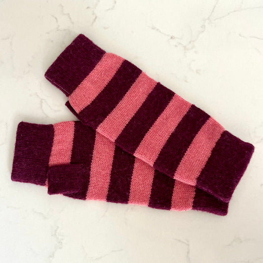 A pair of knitted cashmere wristwarmers with alternating horizontal stripes of deep burgundy and pink, displayed on a light marble surface.