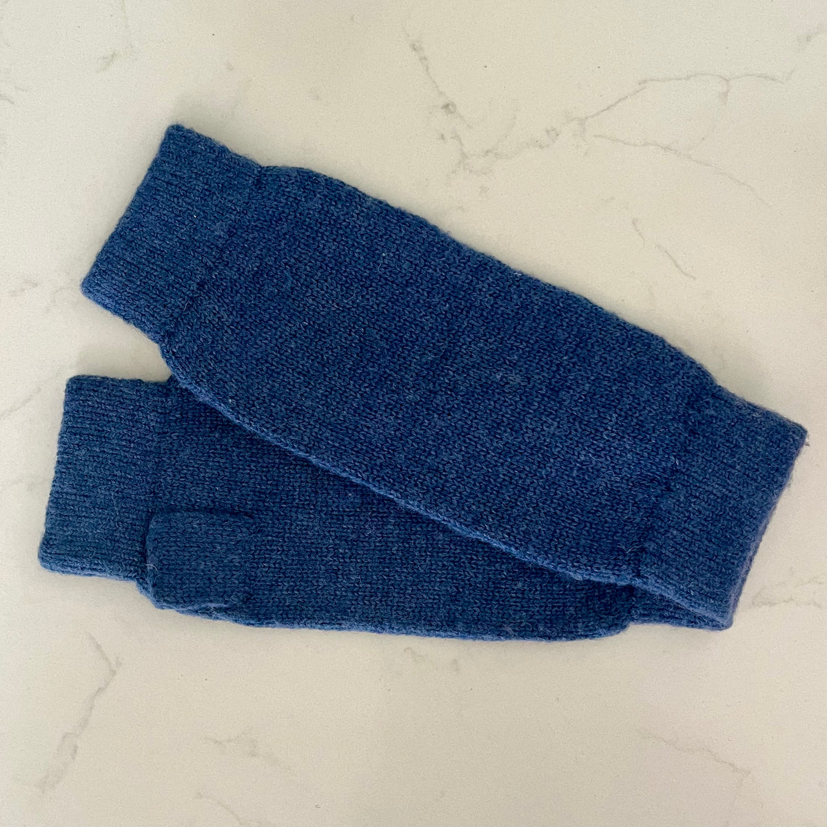 A pair of soft navy blue knitted cashmere wristwarmers laid flat on a light marble surface.