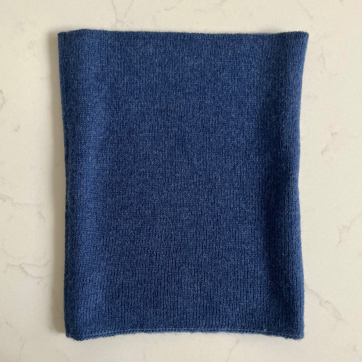 A dark blue kids cashmere snood, laid flat on a light beige marble surface.