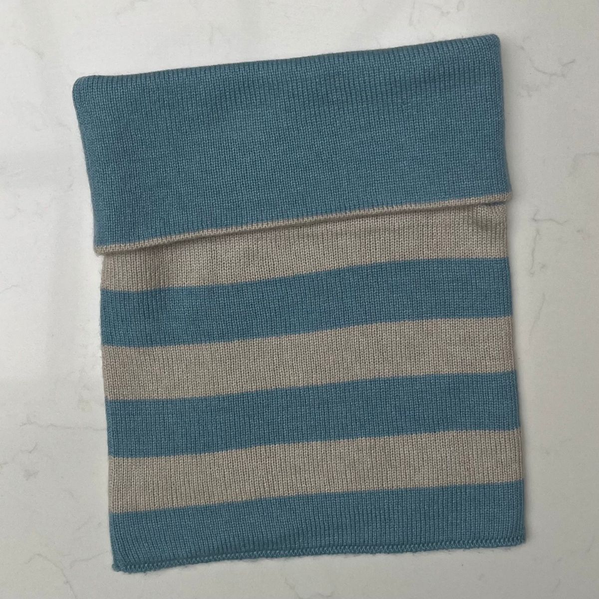 A pretty folded blue and light beige striped cashmere snood on a light gray background