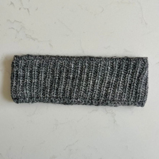 Gray plain knitted woollen headband with a black fleece inner lining on a light gray marble background