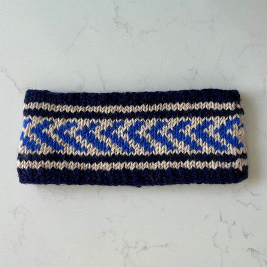 Knitted fleece-lined Saddle Creek headband with a navy, blue and beige pattern on a white marble surface